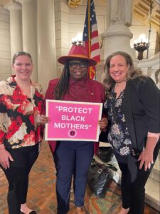 three women smiling and holding up sign that says "Protect Black Mothers"