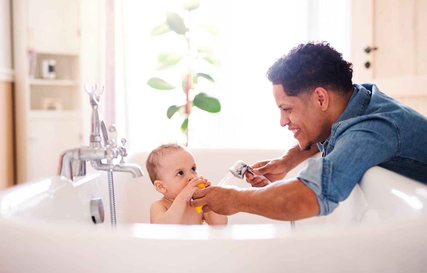 Young man smiling while bathing baby in the tub 